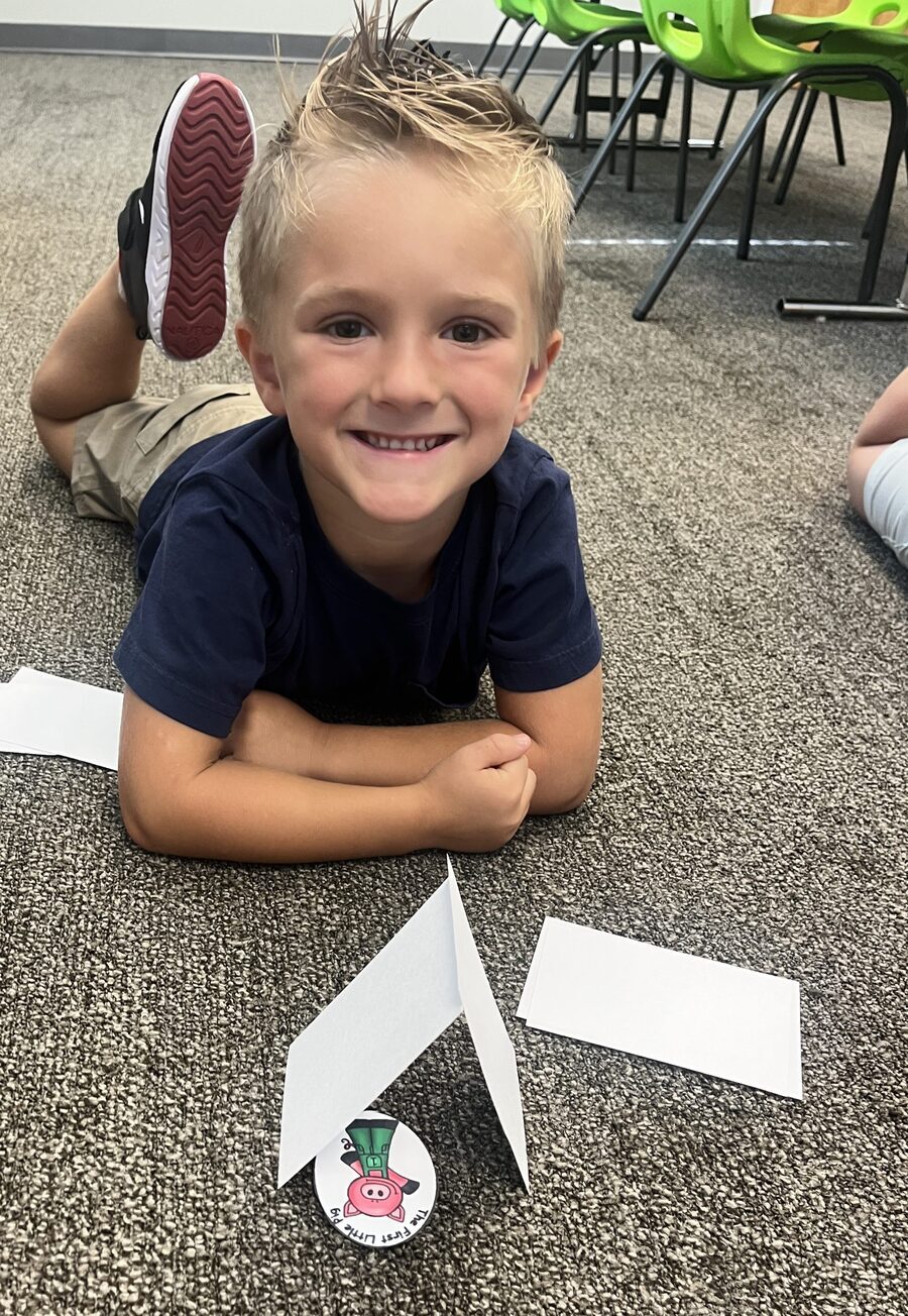 Boy smiling on the floor with a paper airplane he engineered at STEAMCamp