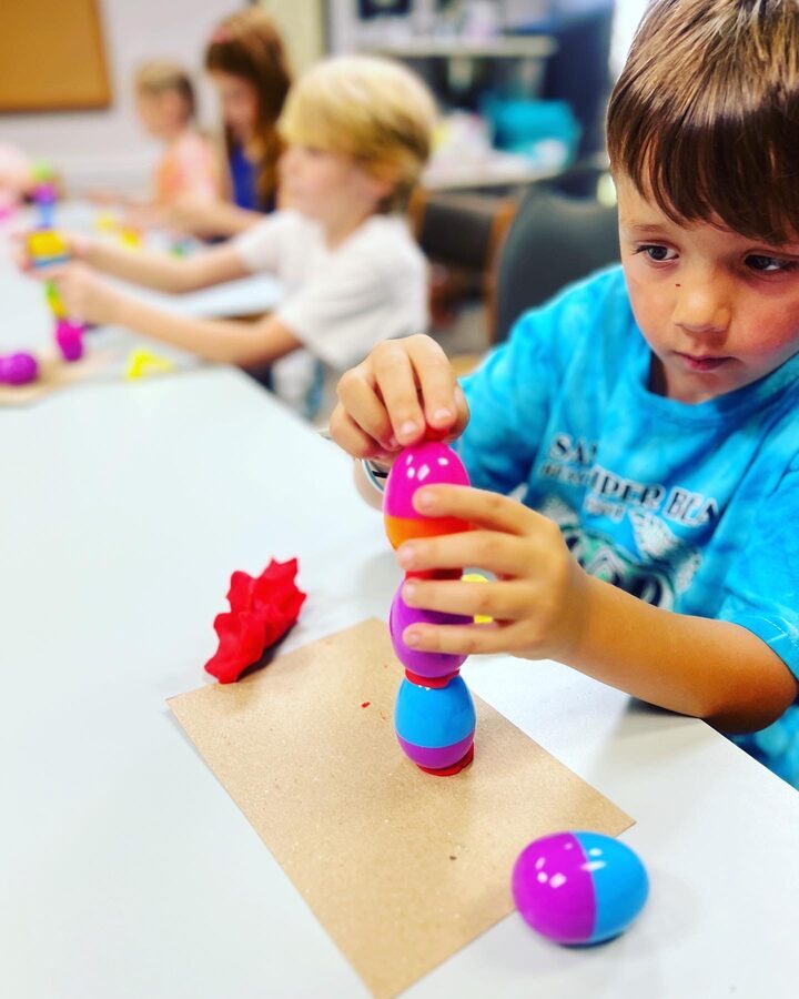 Boy intently stacking colorful plastic eggs in an engineering challenge at STEAMCamp