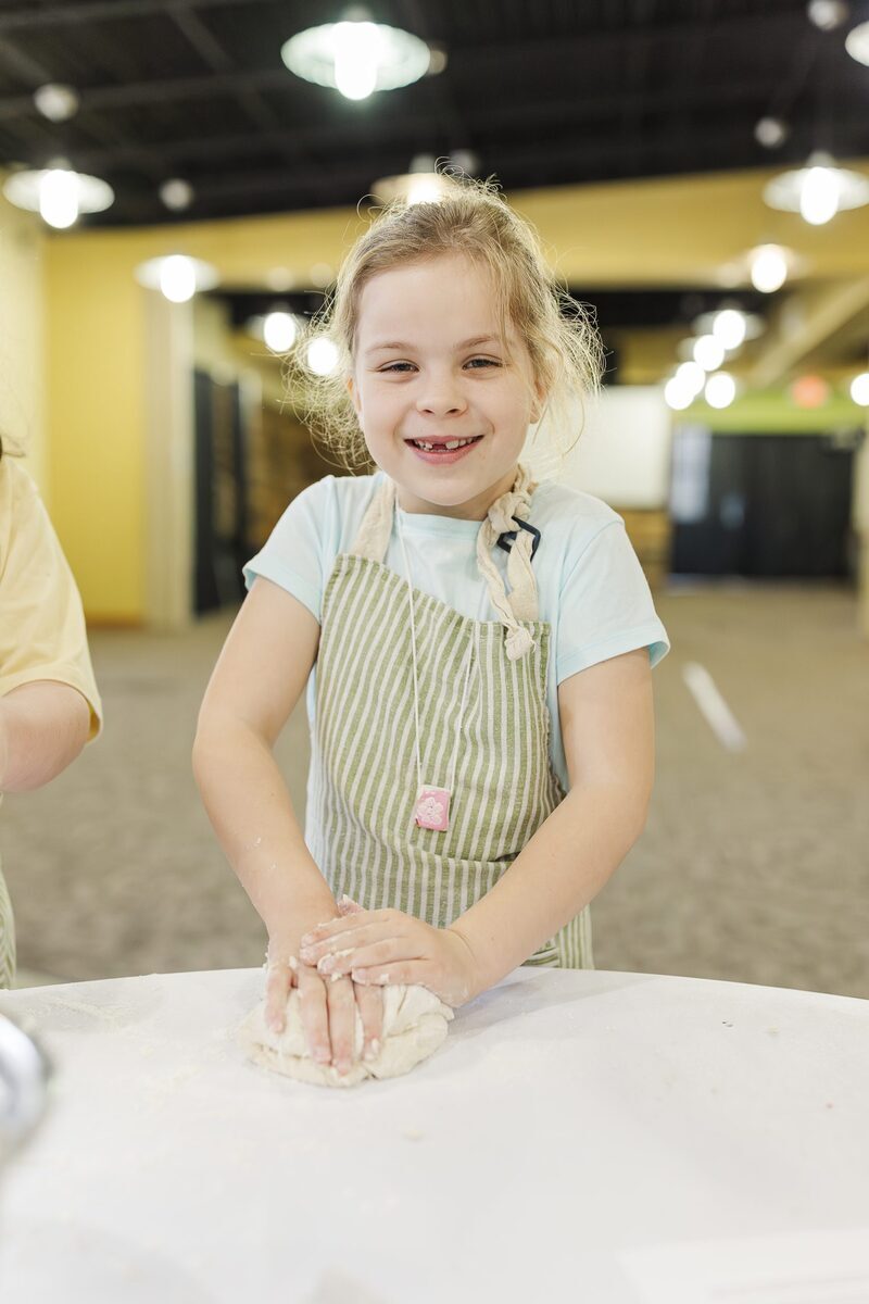 Smiling girl in apron kneading dough during STEAMCamp food science