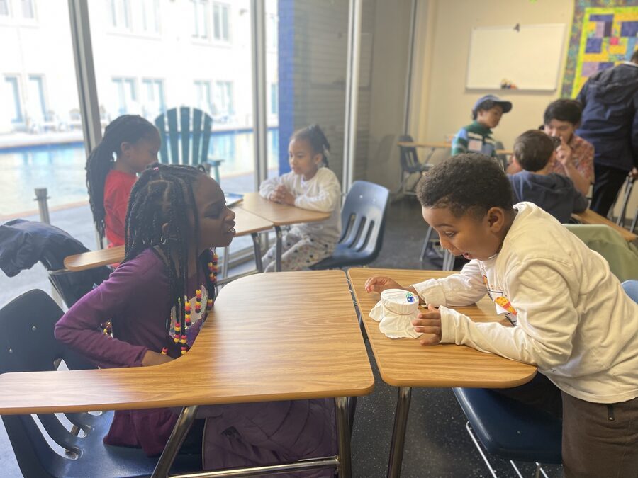 Girl and boy leaning toward each other at desks, intensely focused on a shared project at STEAMCamp
